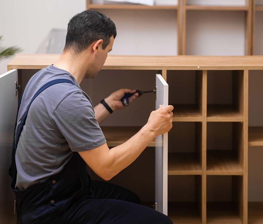 Hombre ensamblando un armario con un destornillador. Puerta blanca y estantería marrón, interior.