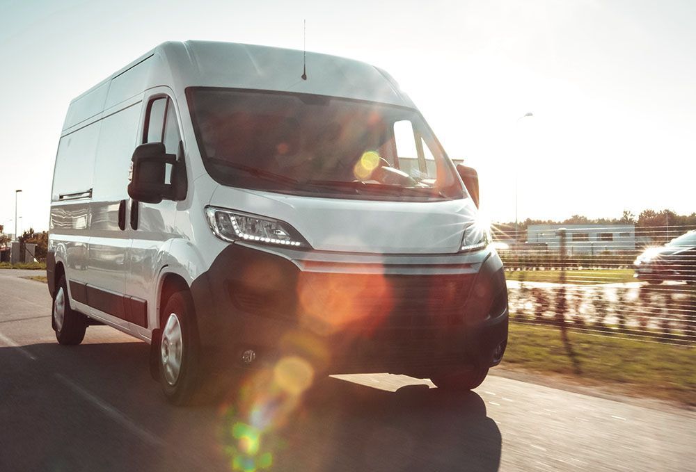 An einem sonnigen Tag fährt ein weißer Lieferwagen eine Straße entlang.