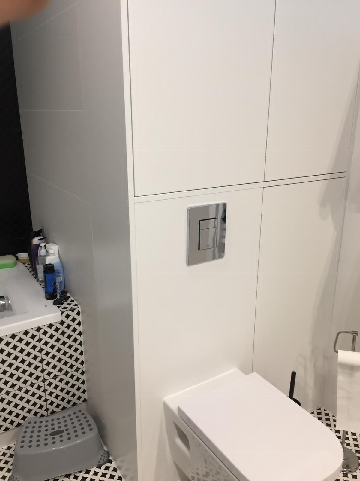 Eine moderne, wandhängende Toilette mit verchromter Zweimengenspülung vor weiß gefliesten Wänden und schwarz-weißen Bodenfliesen.