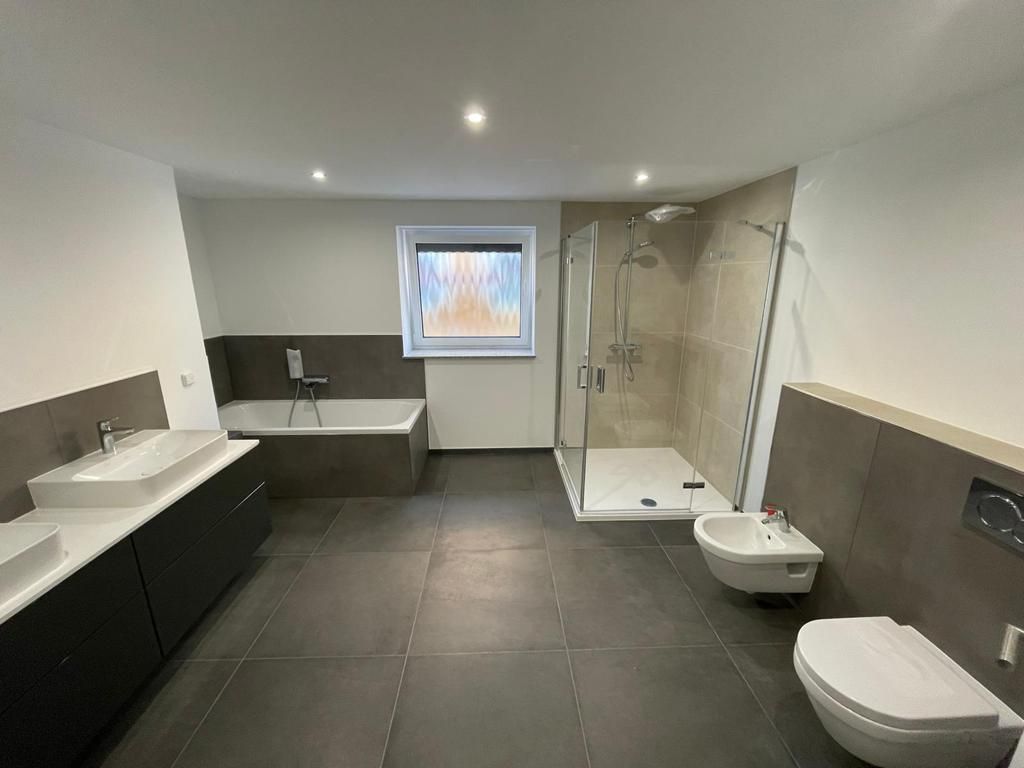 Modernes Badezimmer mit dunklen Bodenfliesen, freistehender Badewanne, begehbarer Glasdusche, weißem Waschtisch und wandhängendem WC.