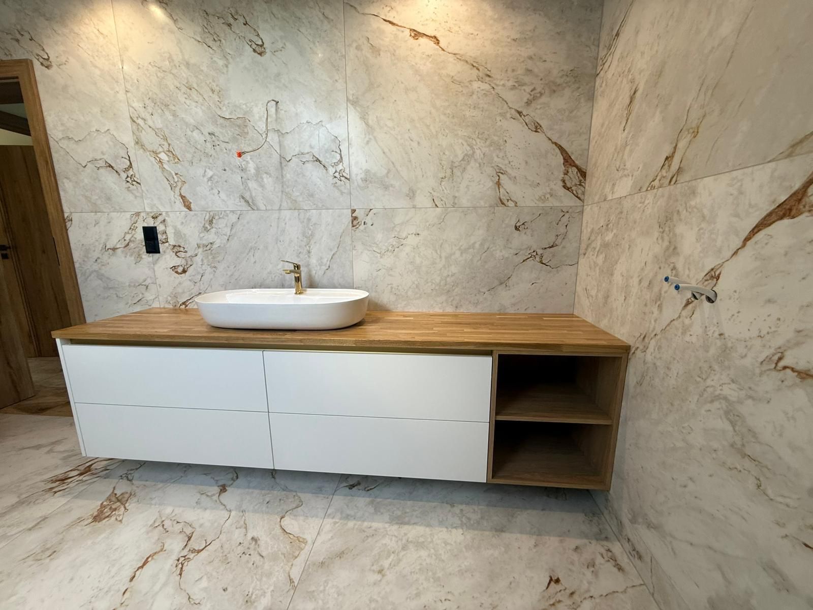 Ein moderner, schwebender Waschtisch mit weißen Schubladen, Holzelementen und einem weißen, ovalen Aufsatzwaschbecken vor einer Marmorwand.