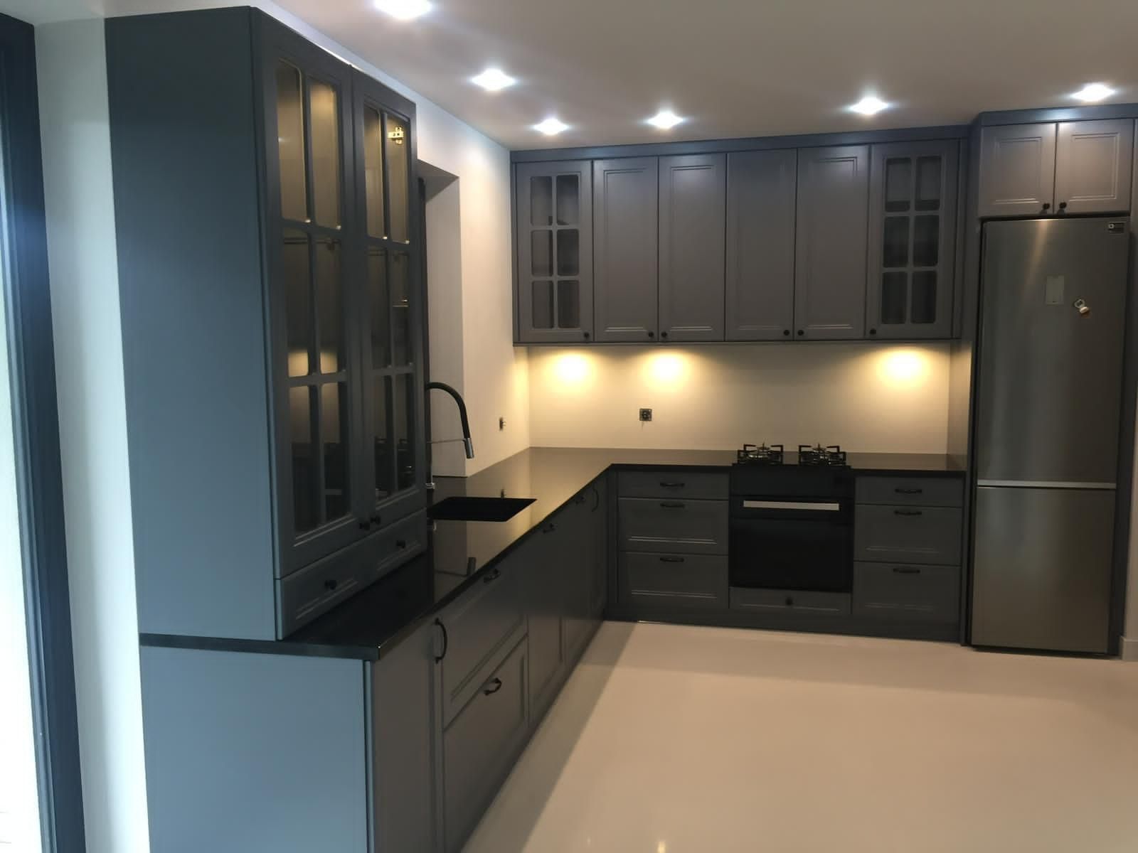 Eine moderne L-förmige Küche mit dunkelgrauen Schränken, schwarzen Arbeitsplatten, Edelstahlgeräten und Unterbaubeleuchtung.