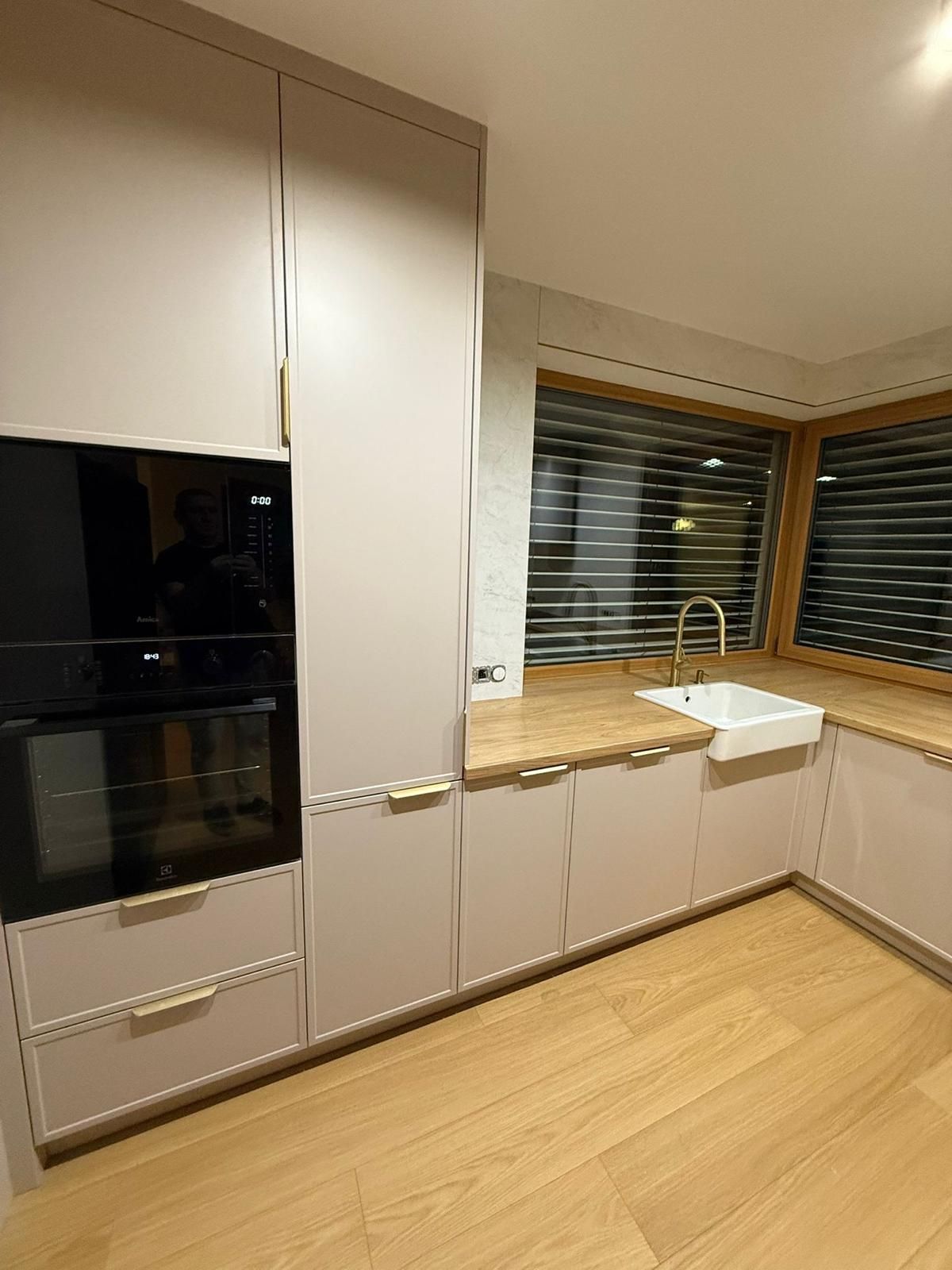 Eine moderne Küche mit hellbeigen Schränken, einem dunklen Einbaubackofen, hellen Holzarbeitsplatten und einer weißen Landhausspüle.