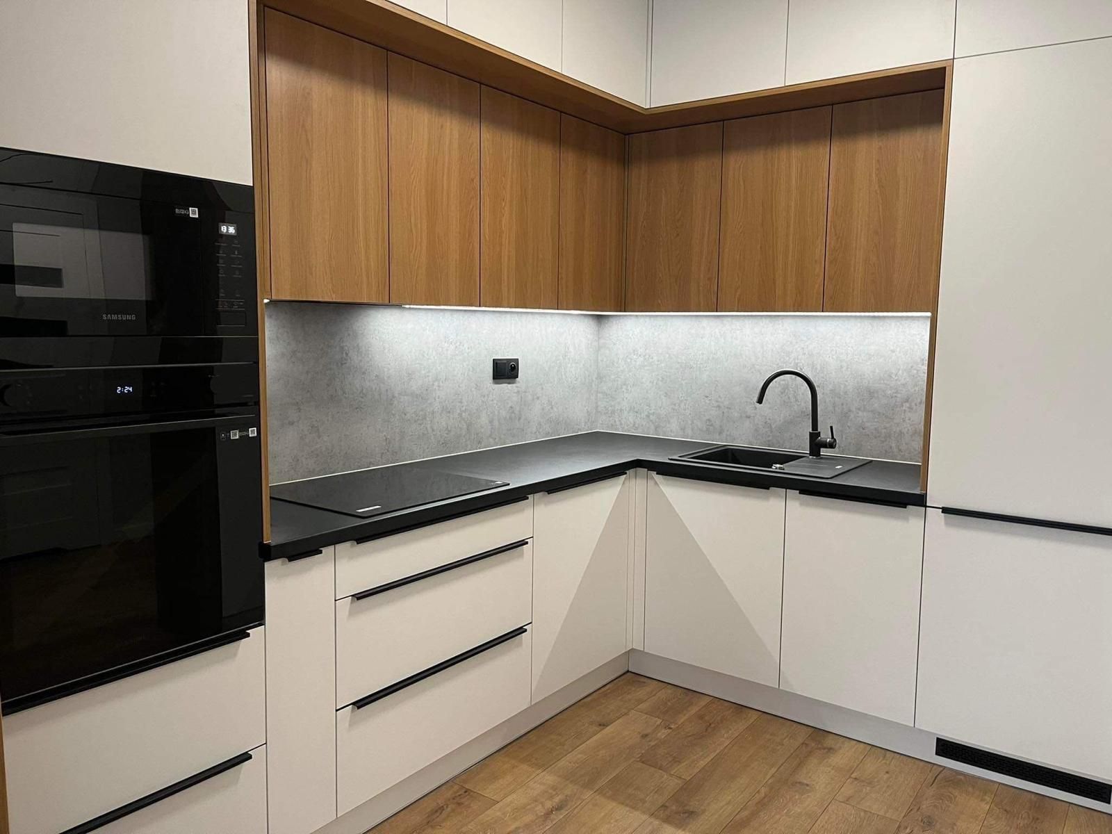 Moderne L-förmige Küche mit weißen Unterschränken, holzfarbenen Oberschränken, schwarzen Elektrogeräten und grauem Fliesenspiegel.