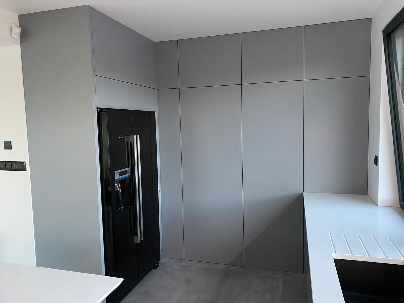 Eine moderne Küche mit einem schwarzen Kühlschrank, der von mattgrauen Schränken und einer weißen Arbeitsplatte eingerahmt wird.