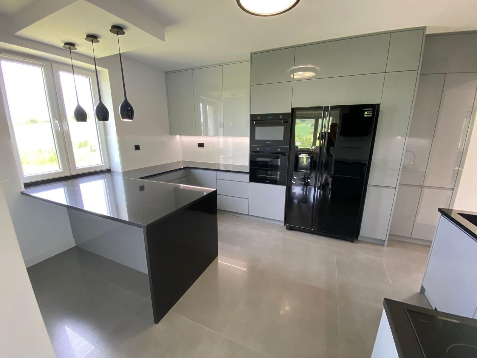 Moderne Küche mit schwarzer Kochinsel, hellgrauen Schränken, schwarzen Elektrogeräten und Pendelleuchten über einer kleinen Theke.