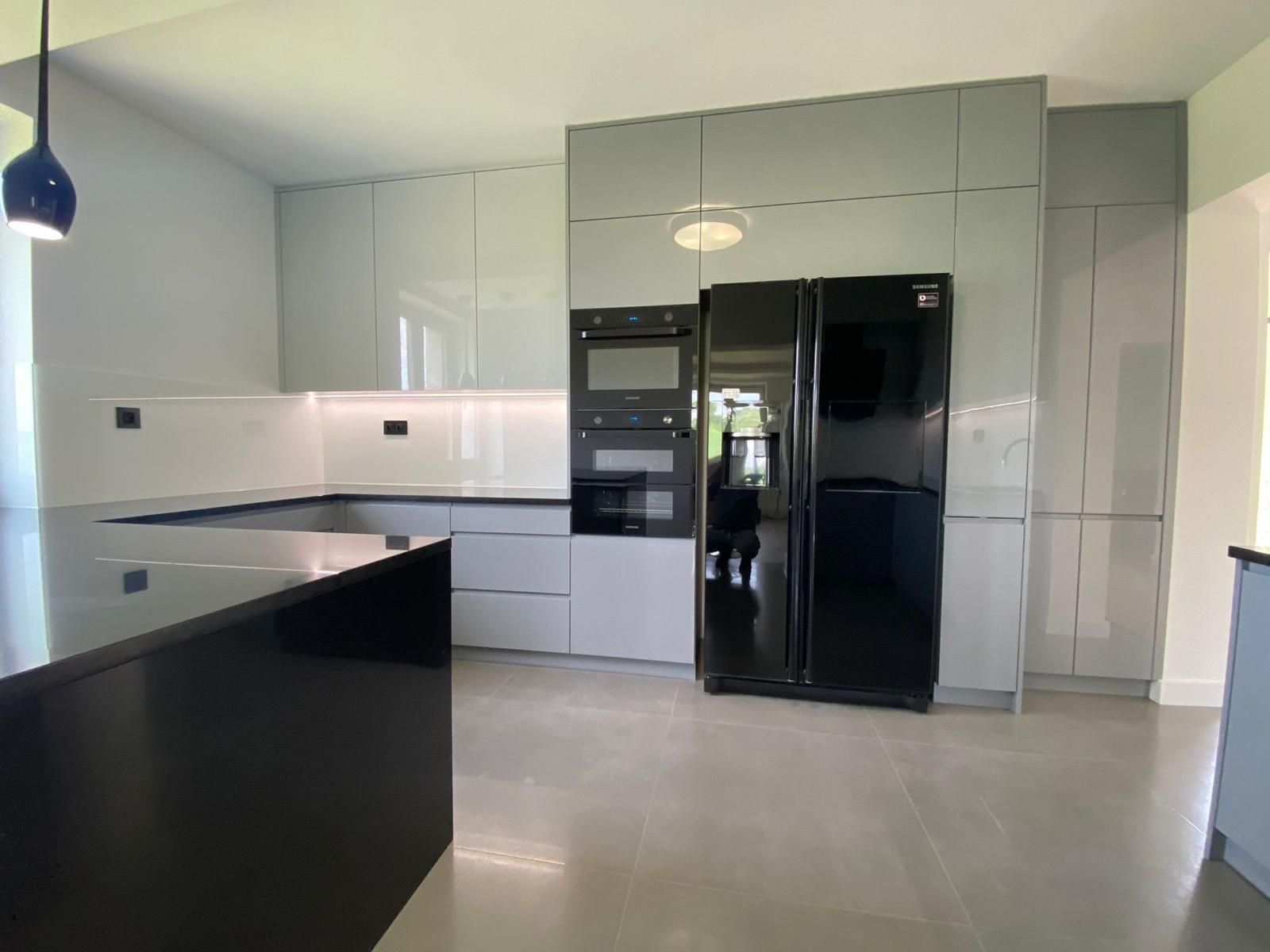 Eine moderne Küche mit glänzend grauen Schränken, einem schwarzen Kühlschrank, Einbaugeräten und einer schwarzen Kücheninsel.