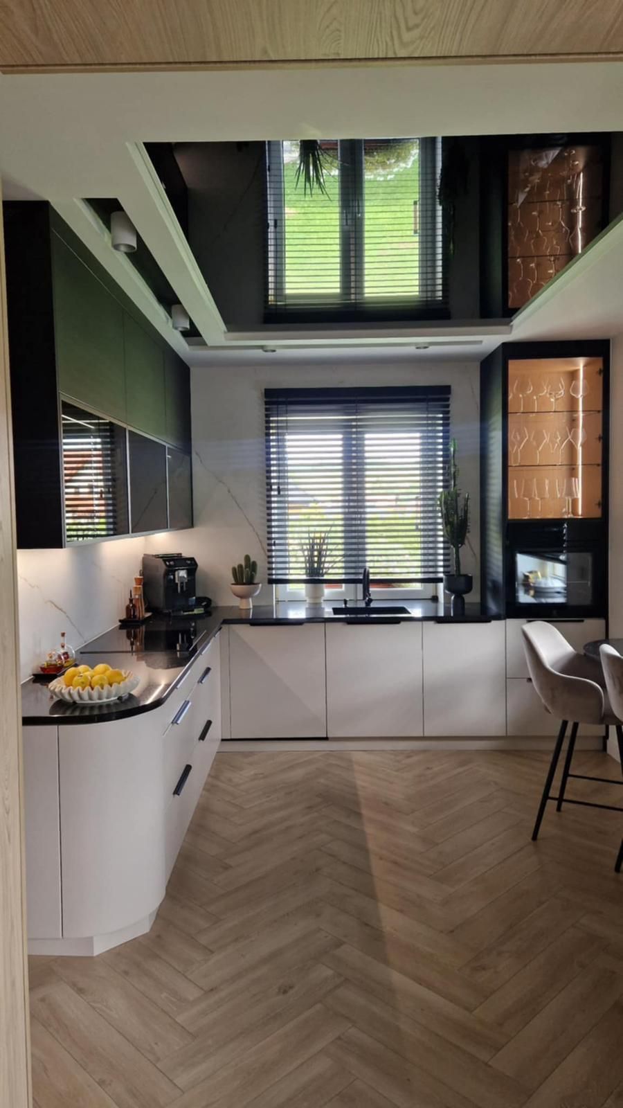 Eine moderne Küche mit weißen Unterschränken, schwarzen Oberschränken, dunklem Fliesenspiegel, einem Fenster und hellem Holzboden.