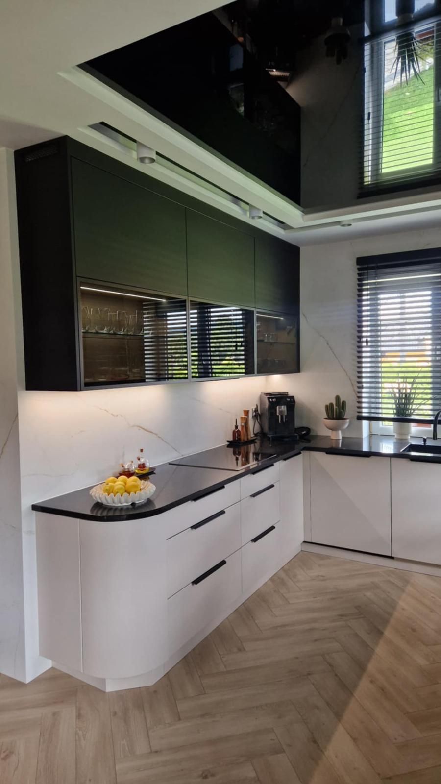 Eine moderne Küche mit mattschwarzen Oberschränken, weißen Unterschränken mit abgerundeten Kanten und hellem Holzboden.