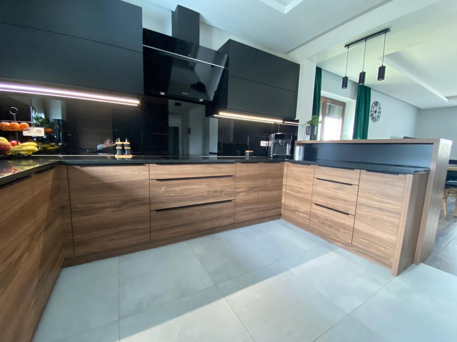 Moderne Küche mit schwarzen Oberschränken, Unterschränken in Holzoptik, dunklem Fliesenspiegel und grauen Fliesenböden.