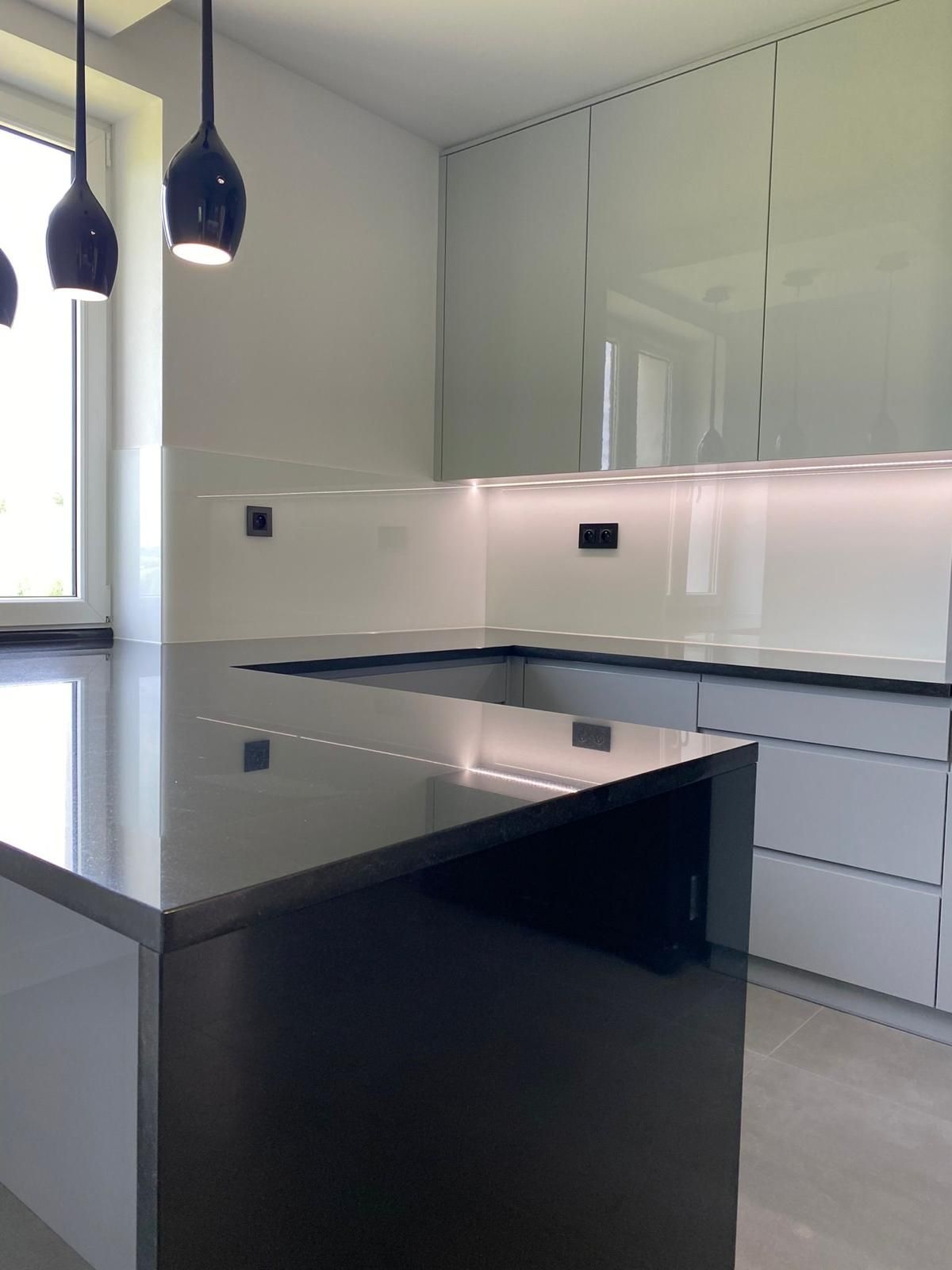 Moderne Küche mit dunkler Kücheninsel, hellgrauen Schränken, eleganter Beleuchtung und weißem Fliesenspiegel.