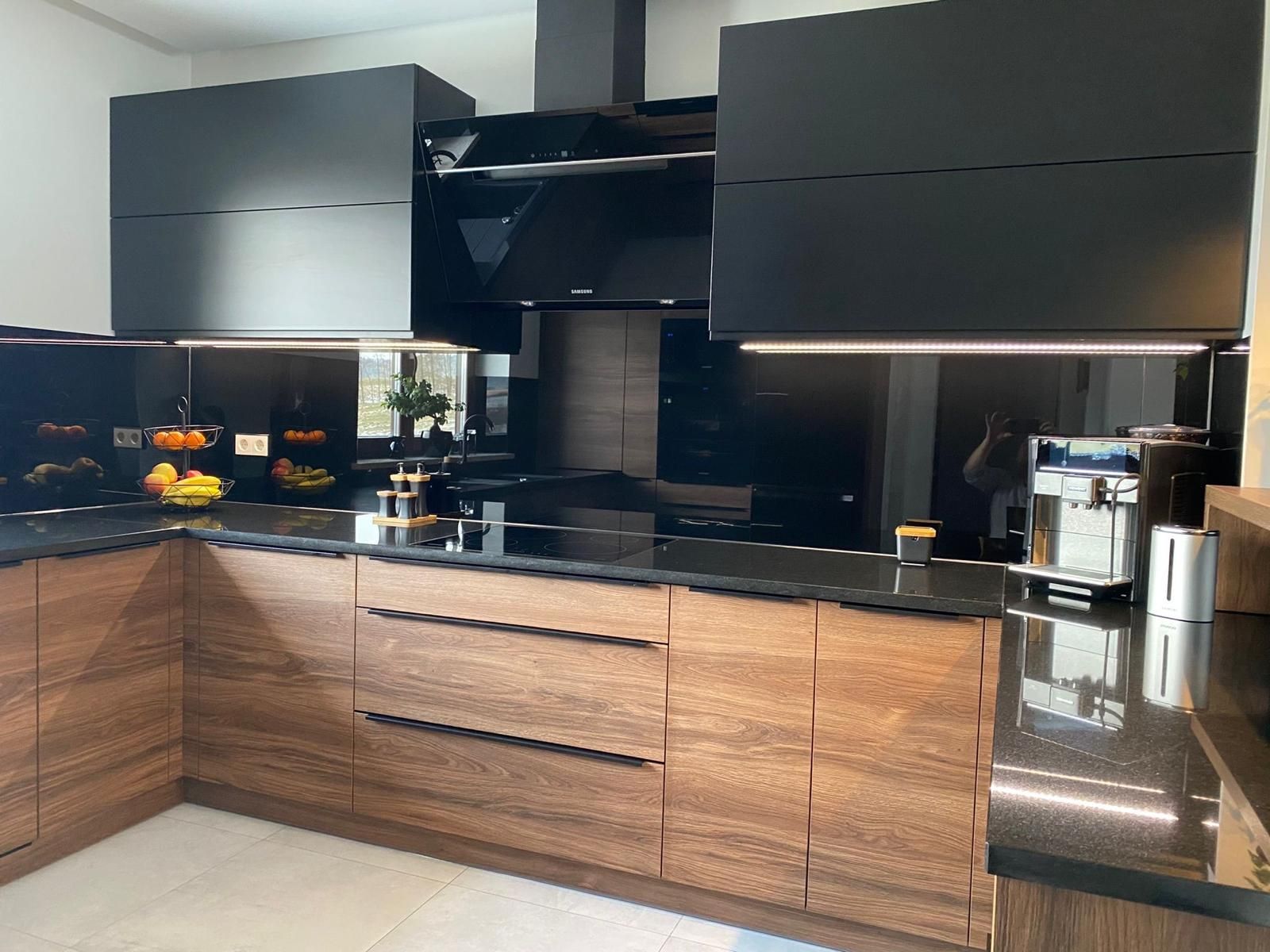 Moderne Küche mit Unterschränken in Holzoptik, schwarzen Hochglanz-Oberschränken, passendem schwarzem Fliesenspiegel und Arbeitsplatten aus Stein.