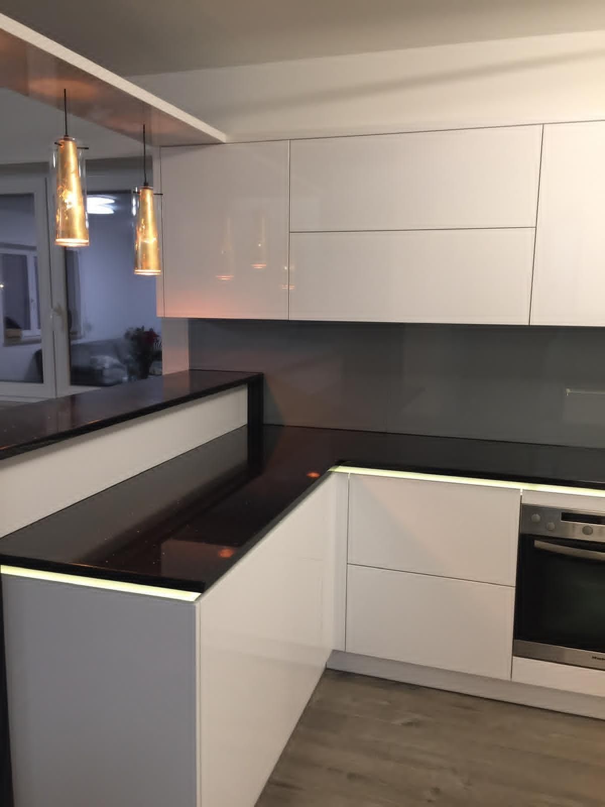 Moderne Küche mit glänzend weißen Schränken, schwarzen Arbeitsplatten, einer Frühstücksbar und zwei Pendelleuchten.