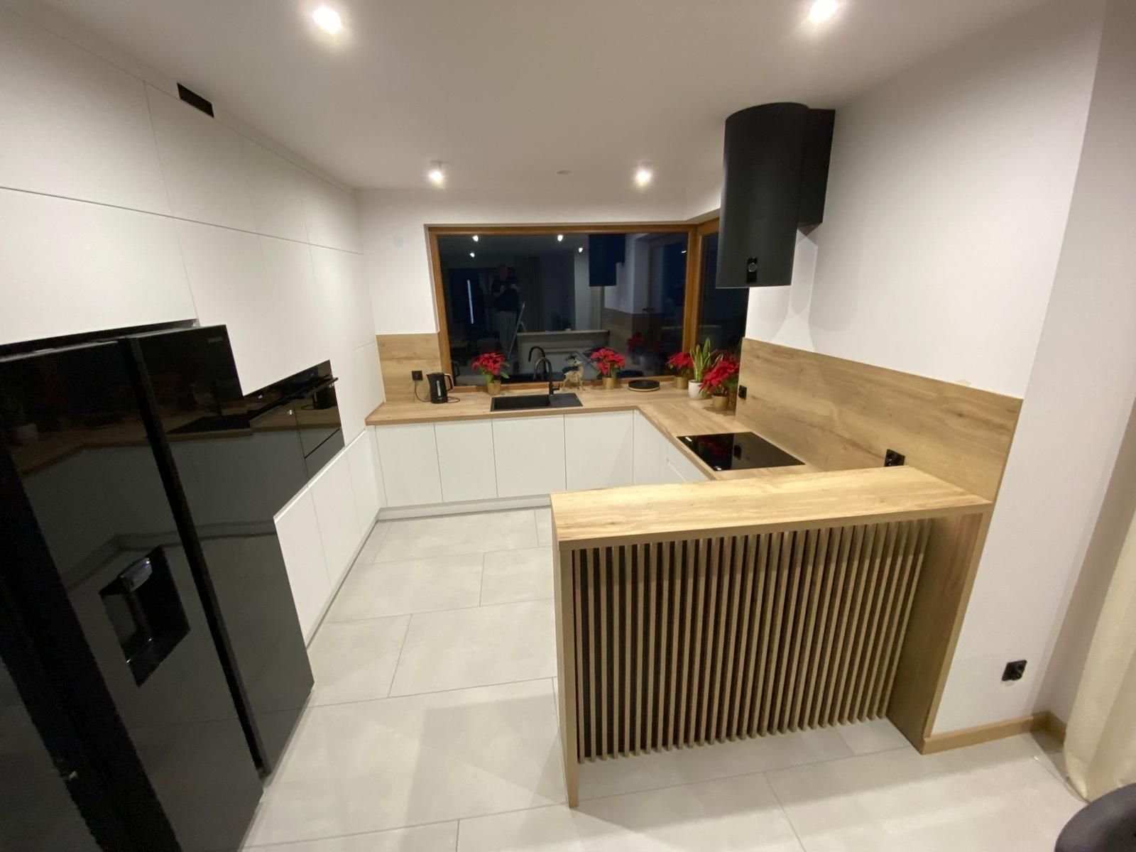 Moderne Küche mit weißen Schränken, hellen Holzarbeitsplatten, einem schwarzen Kühlschrank und einer Frühstückstheke aus Holzlatten.