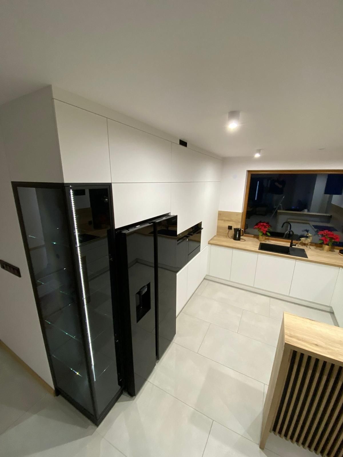 Eine moderne Küche mit weißen Schränken, einem schwarzen Kühlschrank, einer Glasvitrine und hellen Holzarbeitsplatten.