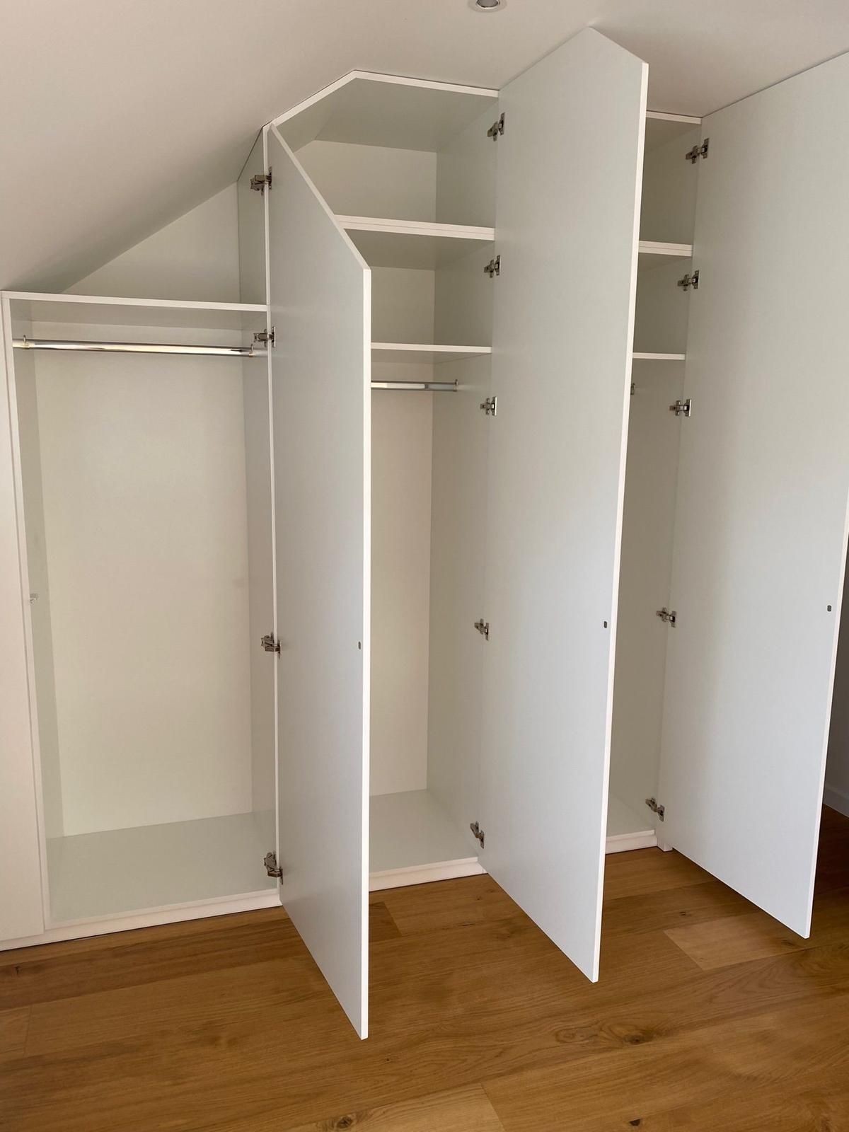Ein mehrteiliger, weißer Einbauschrank mit schrägen oberen Regalböden in einem Zimmer mit Hartholzboden.