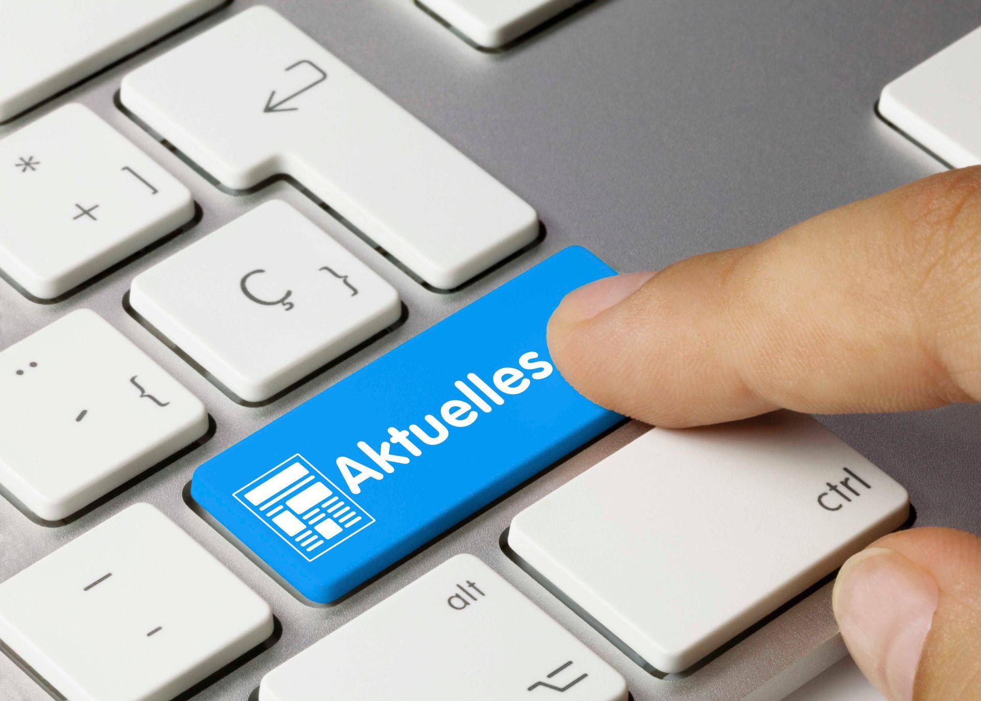Hand drückt eine blaue „Aktuelles“-Taste auf einer Tastatur.