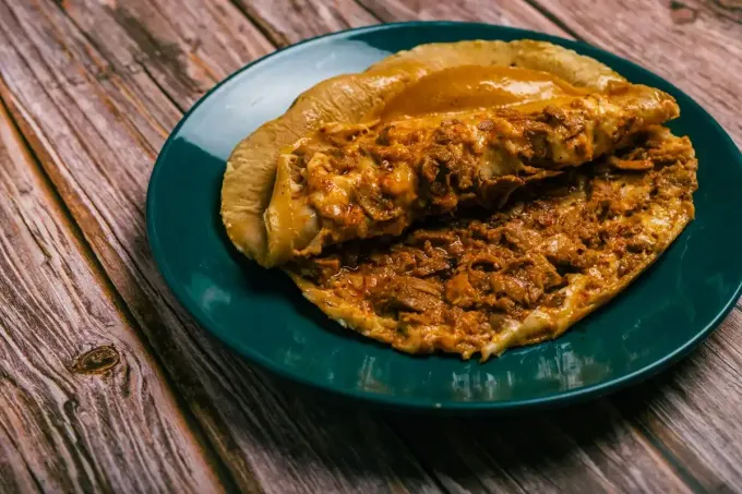 Un sándwich con relleno de carne y salsa en un plato verde azulado, sobre una mesa de madera.
