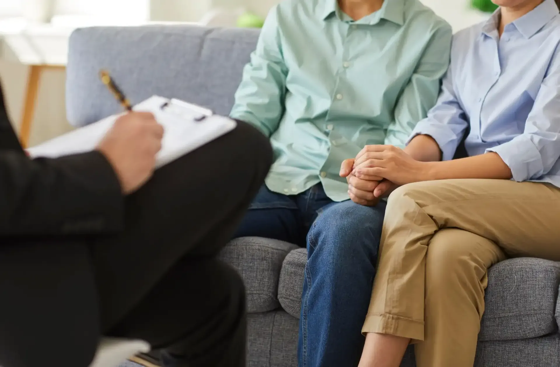 Pareja tomándose de la mano durante una sesión de terapia, el consejero toma notas.