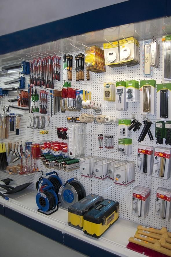 Muro expositor de ferretería con herramientas y accesorios, tablero perforado blanco, varios colores.