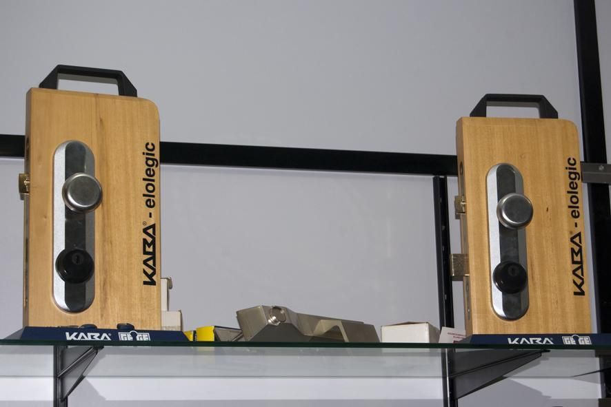 Dos cerraduras de puerta de madera con herrajes plateados y negros exhibidas en un estante con la etiqueta