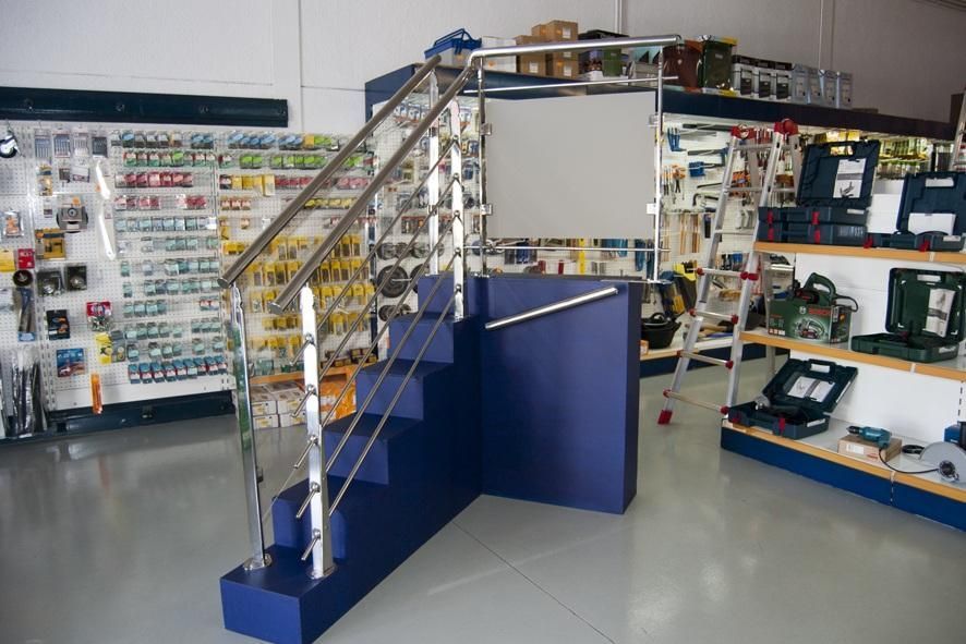 Escalera con pasamanos cromados y contrahuellas azules en una ferretería.