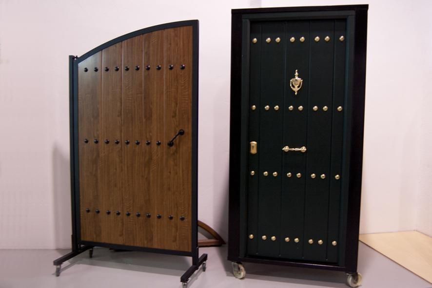 Dos puertas con montantes: una arqueada, de madera y de color marrón; la otra verde, rectangular y con aldaba.