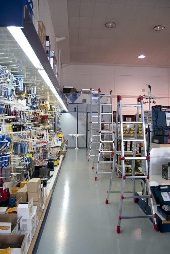Pasillo de ferretería con estantes de herramientas y múltiples escaleras.