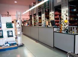 Interior de una ferretería con herramientas y estantes detrás de un largo mostrador gris.