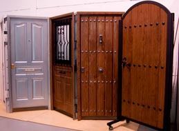 Tres puertas de madera diferentes en exhibición en una sala de exposición, que varían en estilo y color.