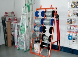 Estante naranja con carretes de cadena en una ferretería. Se ven escaleras detrás.