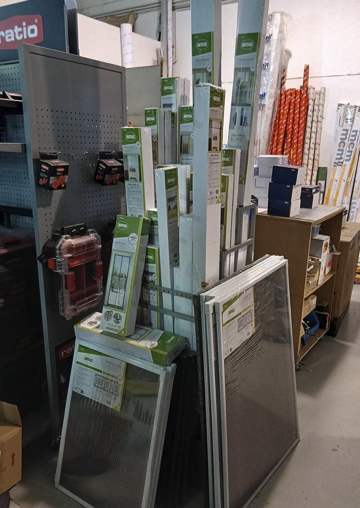 Pasillo de la tienda con mosquiteras y marcos apilados en la sección de ferretería.