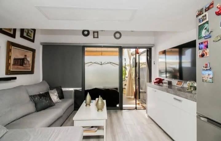 Salón con sofá gris, mesa blanca, puerta corredera y televisor de pared.