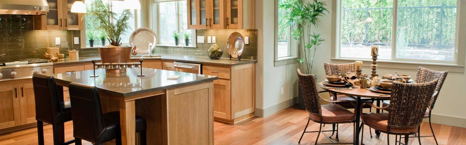 Una cocina con armarios de madera clara, una isla oscura con taburetes y un comedor con una mesa redonda y sillas.