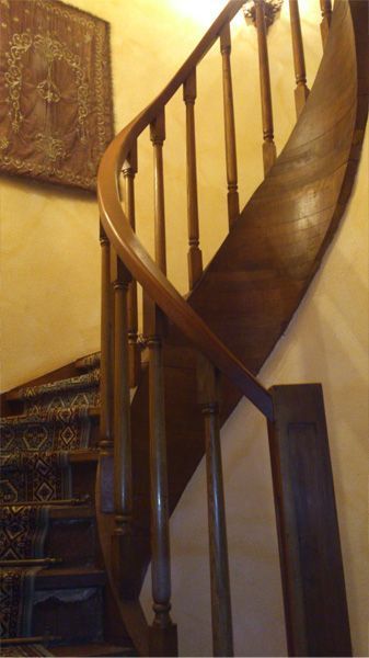 Una escalera curva de madera con barandillas oscuras y una alfombra estampada, contrastando con una pared de tonos cálidos adornada con cuadros enmarcados.