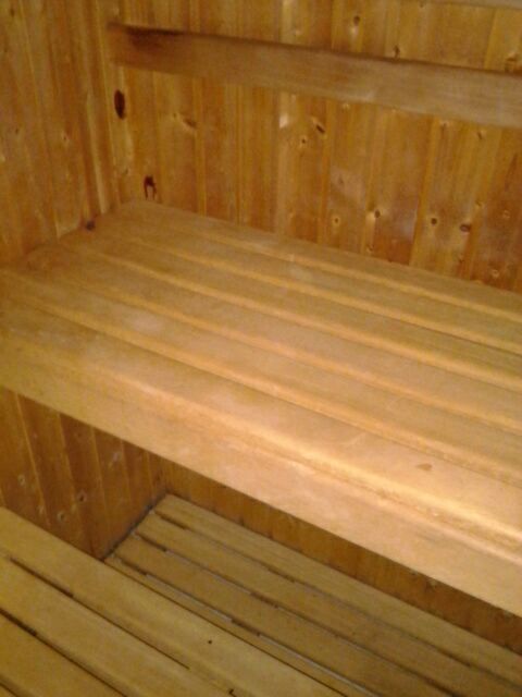 Primer plano de bancos de sauna de madera de color claro con listones horizontales, contrastando con las paredes revestidas de paneles de madera a juego.