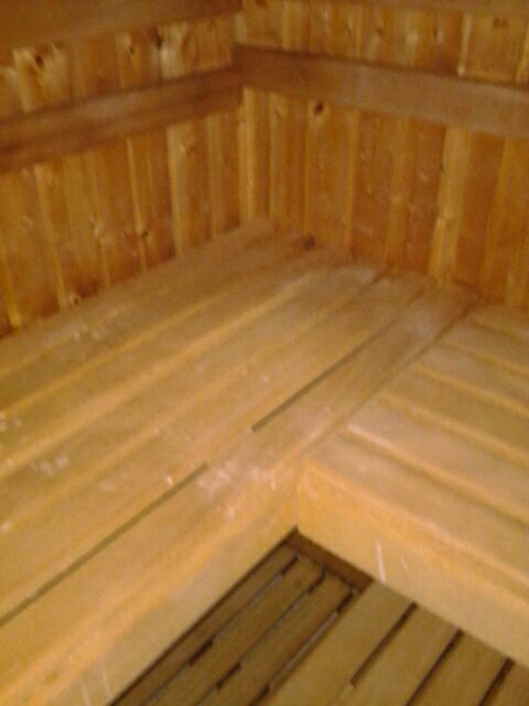 Un rincón interior de una sauna con bancos y paredes revestidos de listones de madera de color claro.