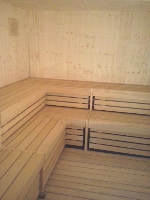 Una sala de sauna vacía con bancos de listones de madera de color claro dispuestos en forma de L a lo largo de las paredes.