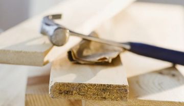 Un martillo de orejas descansa sobre varias tablas de madera apiladas y un trozo de papel marrón arrugado.