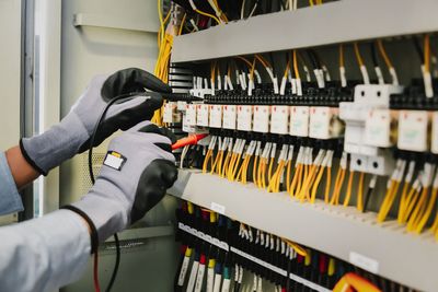 Behandschuhte Hände verkabeln einen Serverschrank mit gelben und schwarzen Kabeln in einem Verteilerkasten.