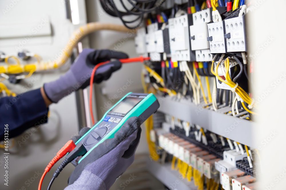 Techniker prüft die elektrische Verkabelung in einem Schaltschrank mit einem digitalen Messgerät.