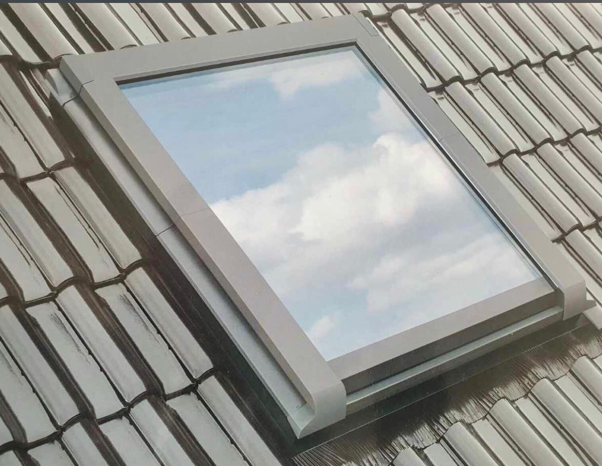 Ein Dachfenster auf einem Ziegeldach spiegelt den bewölkten Himmel wider.