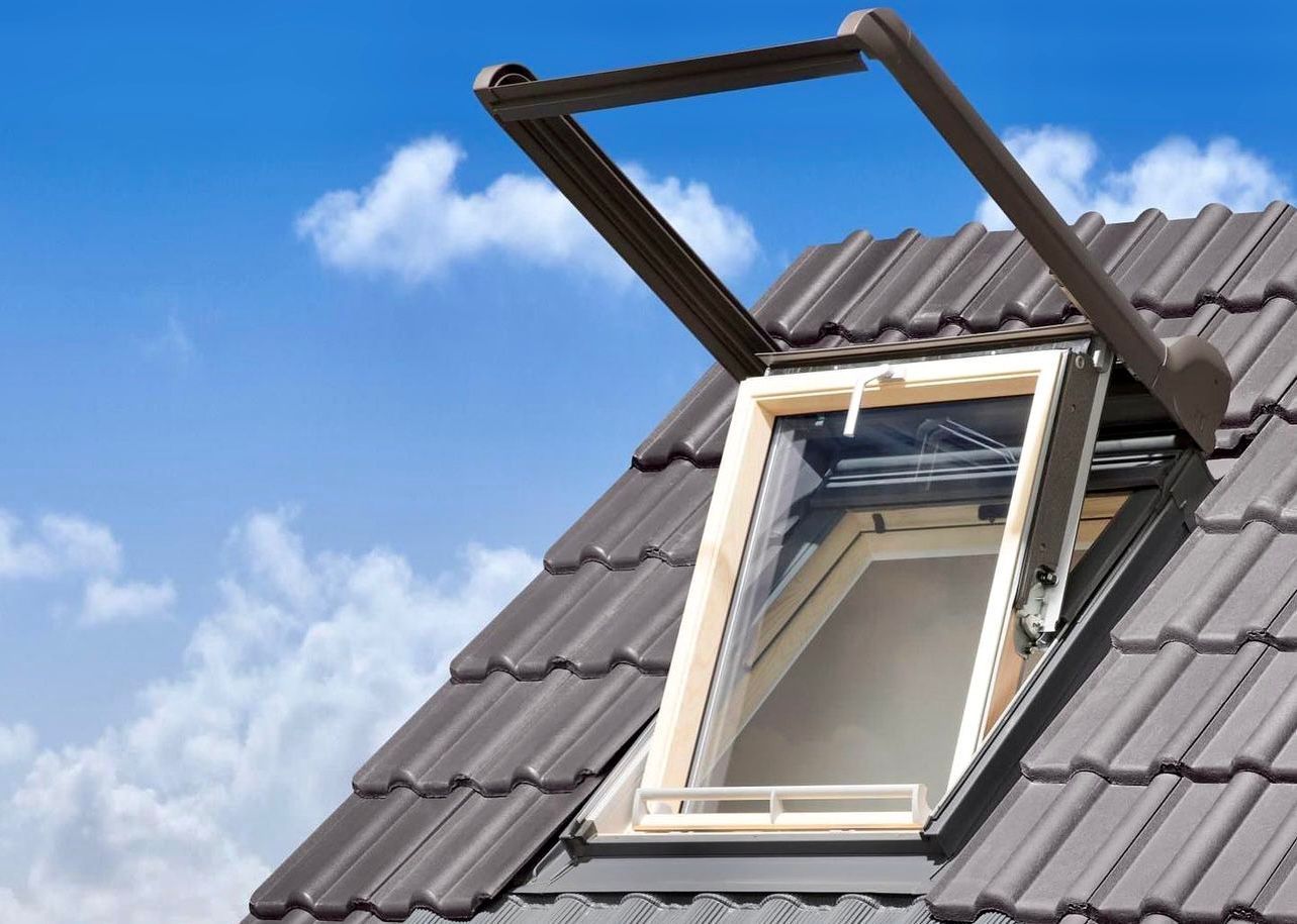 Offenes Dachfenster auf einem Ziegeldach vor blauem Himmel mit Wolken.