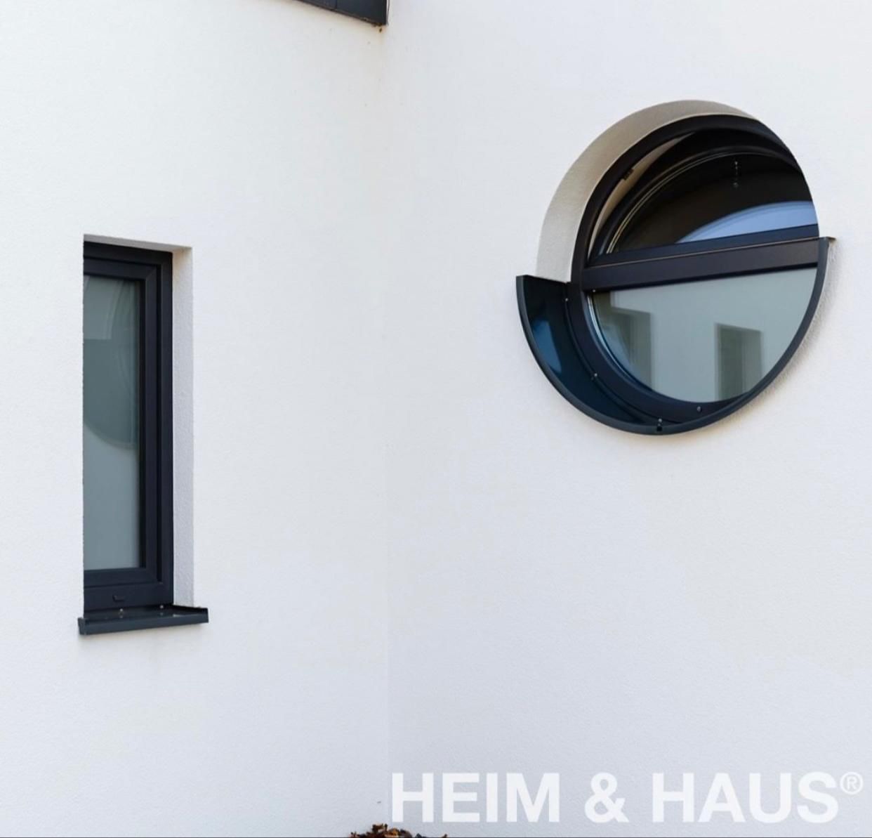 Außenecke eines weißen Gebäudes mit zwei dunkel gerahmten Fenstern; eines rechteckig, das andere ein Halbkreis.