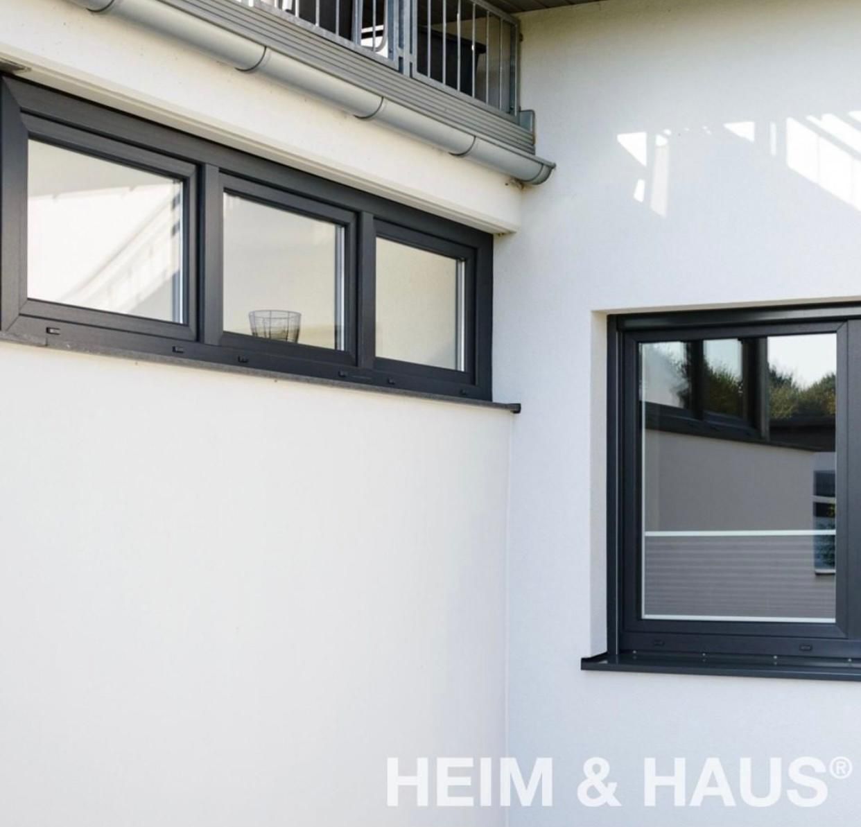 Außenansicht eines weißen Gebäudes mit dunkel gerahmten Fenstern; darüber ist ein Balkon zu sehen.