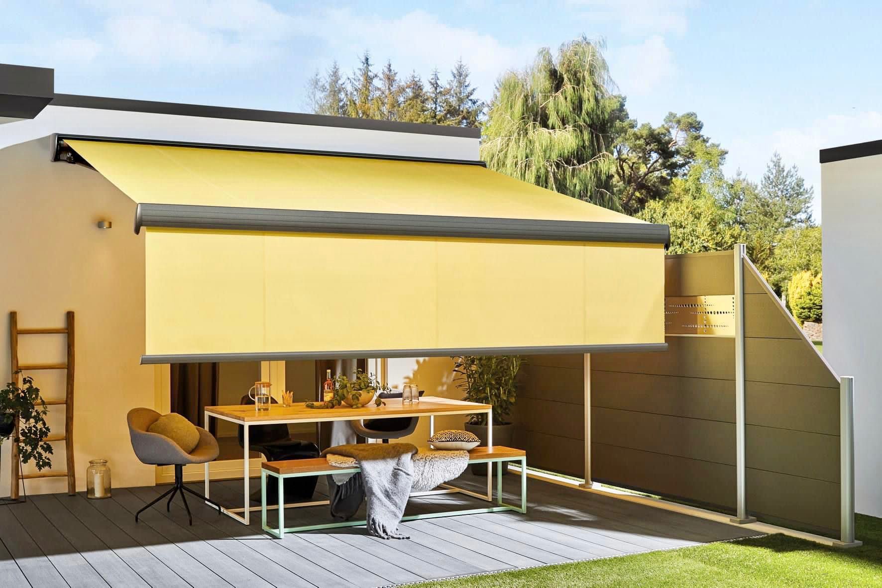 Eine gelbe Markise spendet Schatten über einer Essgruppe auf der Terrasse.