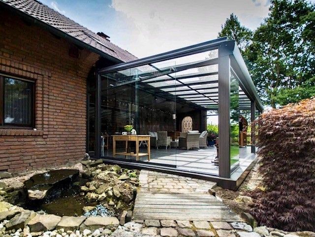 Verglaster Wintergarten an einem Backsteinhaus mit Sitzgelegenheiten und einem kleinen Teich in der Nähe.