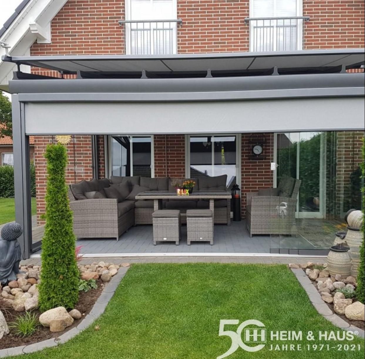 Terrasse mit grauen Möbeln, ausfahrbarer Markise, Glaswänden und kleinem Garten.