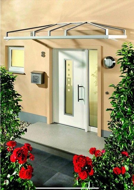 Weiße Eingangstür mit Glaseinsatz unter einer silbernen Markise. Rote Rosen und grüne Sträucher rahmen den Eingang ein.