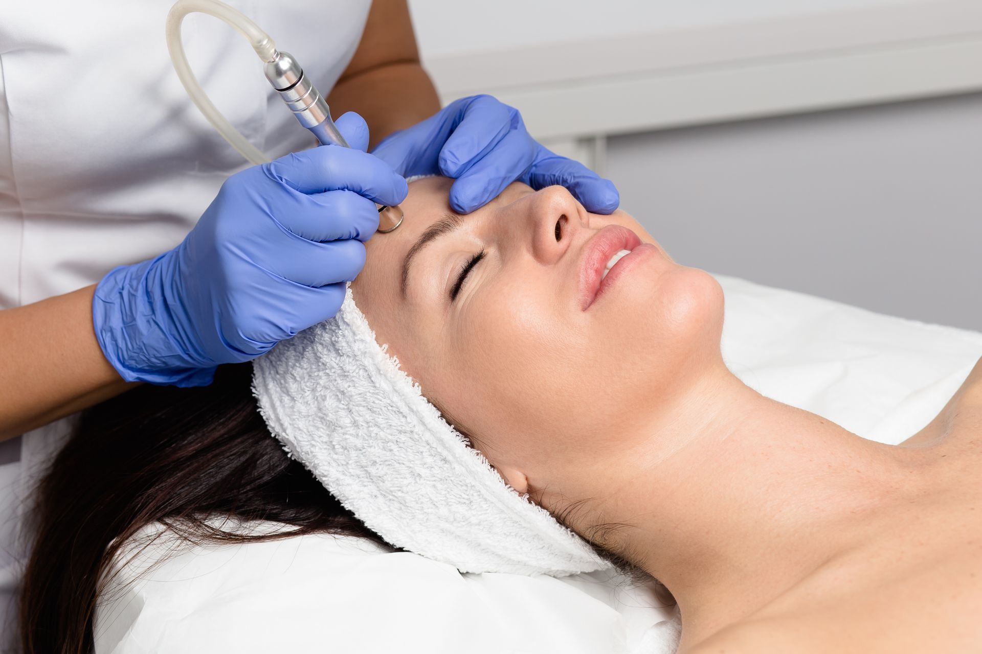 Un praticien ganté effectue un traitement de microneedling facial sur un patient allongé.